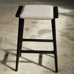 Sitio Stool in natural wood finish used as a seat beside a sofa in a minimalist living room