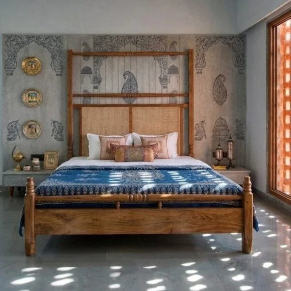 Royal wooden bed with cane headboard placed in a heritage-style bedroom with artistic wall patterns and natural sunlight.