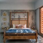 Royal wooden bed with cane headboard placed in a heritage-style bedroom with artistic wall patterns and natural sunlight.