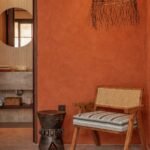 Cane wooden lounge chair with striped cushion placed against a terracotta wall with hanging lamp and rustic decor.