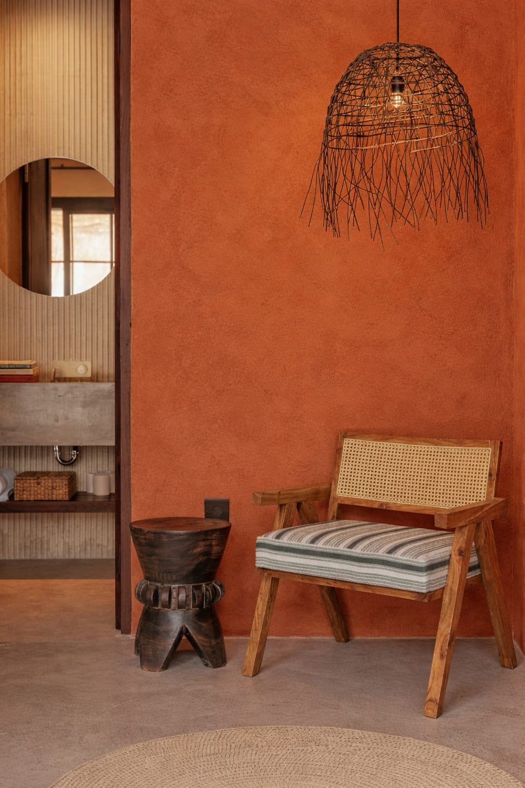 Cane wooden lounge chair with striped cushion placed against a terracotta wall with hanging lamp and rustic decor.
