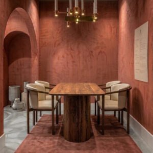 Modern walnut dining table with a fluted pedestal base and four cream upholstered chairs in a room with terracotta textured walls.