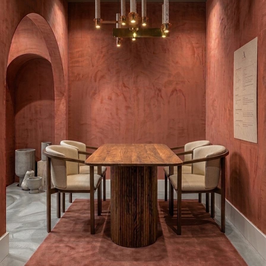 Modern walnut dining table with a fluted pedestal base and four cream upholstered chairs in a room with terracotta textured walls.