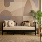 Aria Cane Sofa with black wooden frame, curved cane-woven backrest and armrests, and beige upholstered seat.