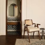 Auro Cane Chair with walnut-tone wooden frame, natural woven cane backrest, rounded wooden armrests, and cream upholstered seat.