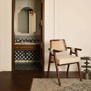 Auro Cane Chair with walnut-tone wooden frame, natural woven cane backrest, rounded wooden armrests, and cream upholstered seat.